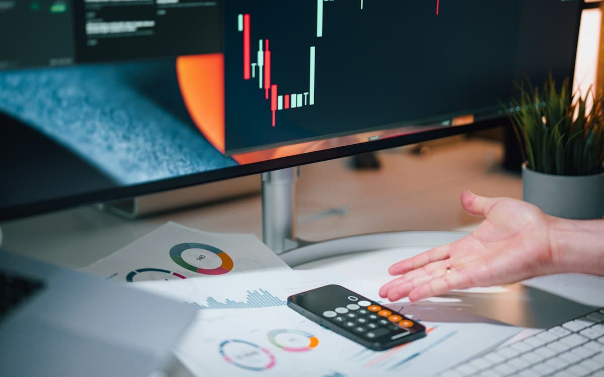 Mesa de escritório com calculadora, relatórios e gráficos no monitor