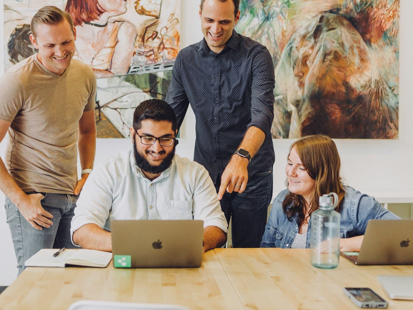 Colegas de trabalho sorrindo em volta de um notebook no escritório